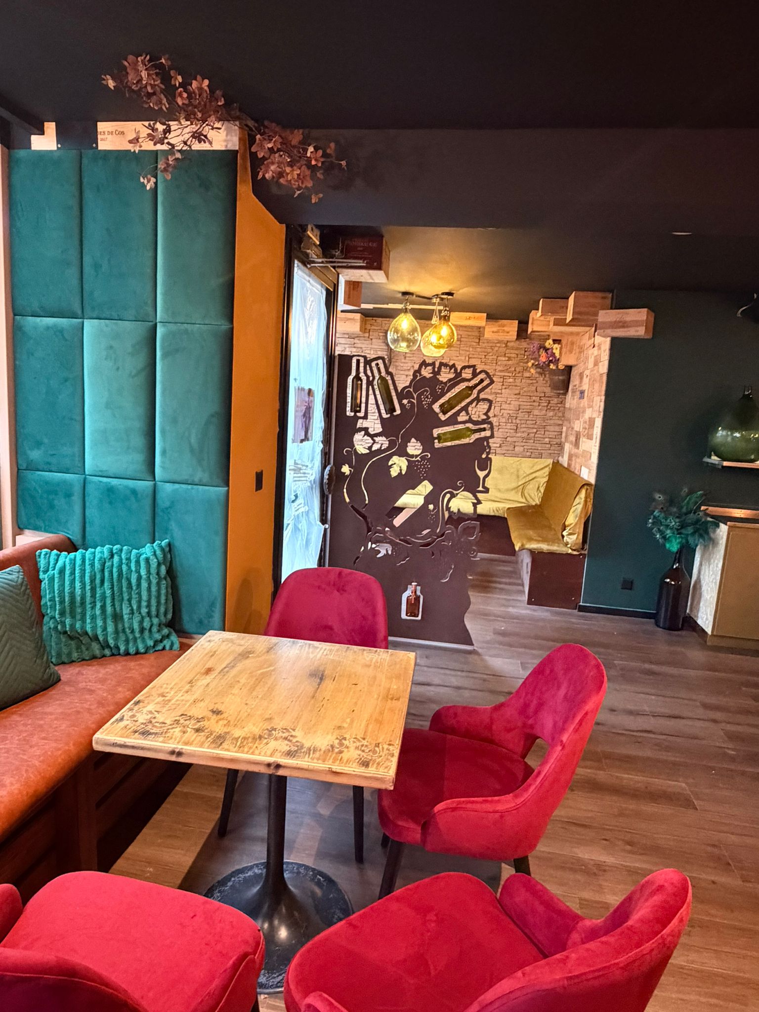 Espace lounge d'Origen Riviera avec mur bleu-vert capitonné, table en bois et assises rouges.